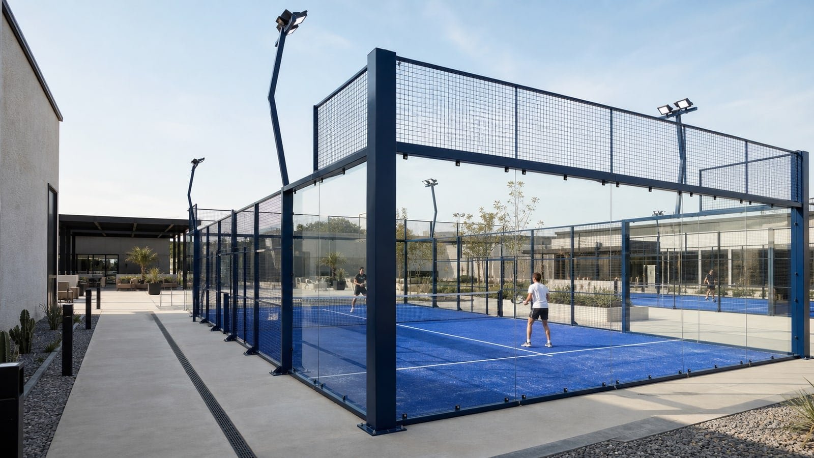 Outdoor padel facility with blue-turf courts, glass enclosures and steel lighting structures.